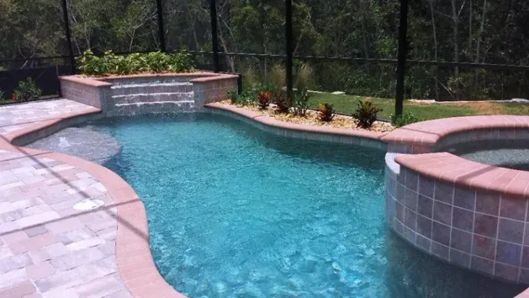 A freeform pool with a tiled spa spillway on a wooded lot