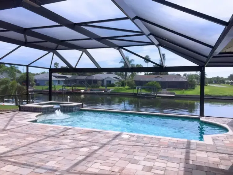 Canal-front screened pool with a raised spa, a dock visible beyond the cage