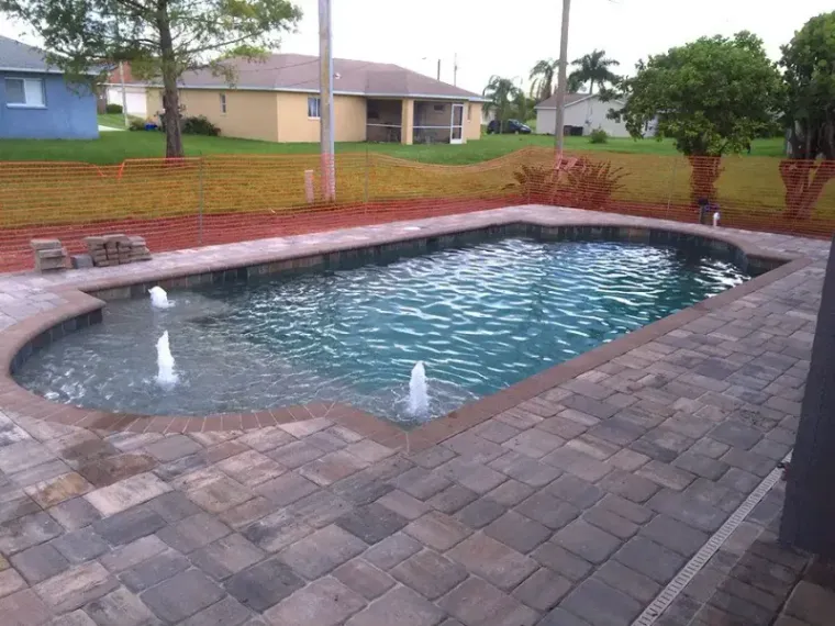 Pool under construction with safety fencing, exposed pavers and two deck jets running